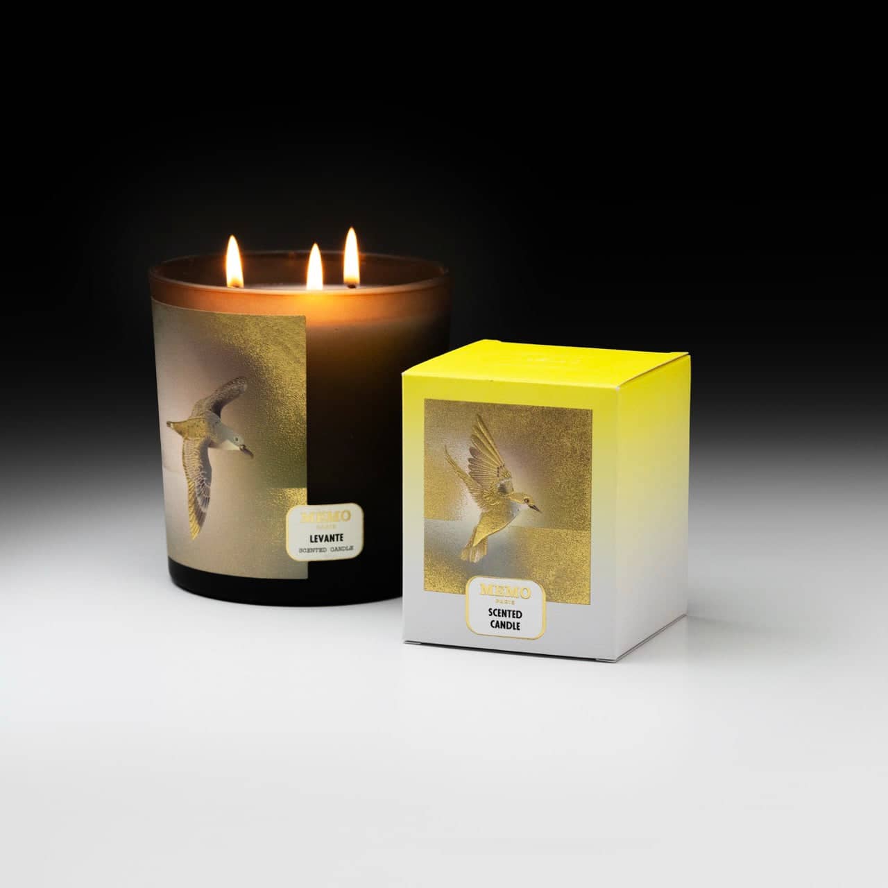 A lit, amber glass scented candle with three wicks and a printed image of a seagull on its side.