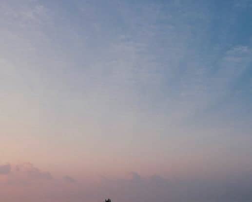 A silhouette of a lone figure standing against a soft gradient sky transitioning from pink to blue.