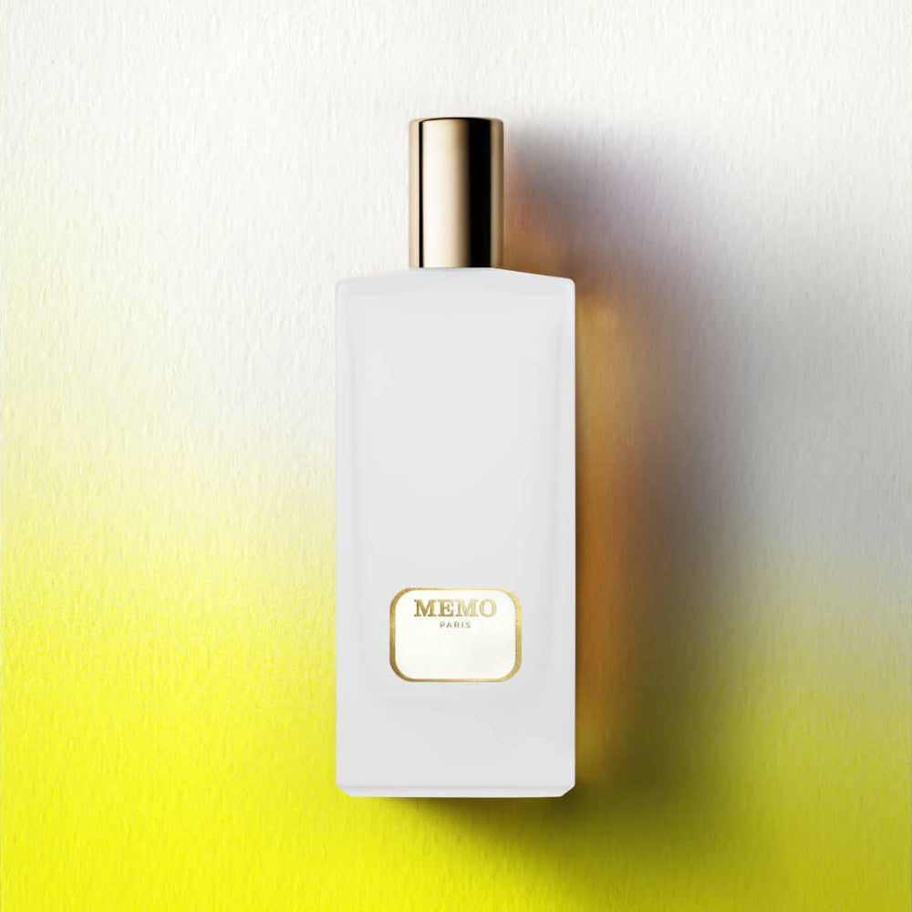 A sleek white rectangular perfume bottle with a gold cap and a minimalist gold label reading ’memo paris.’
